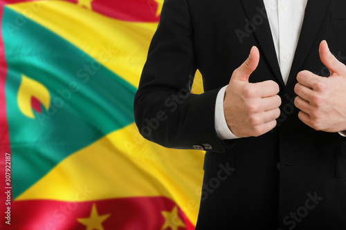Grenada businessman showing thumbs up behind country flag with copy space. Successful international relations and agreement concept.