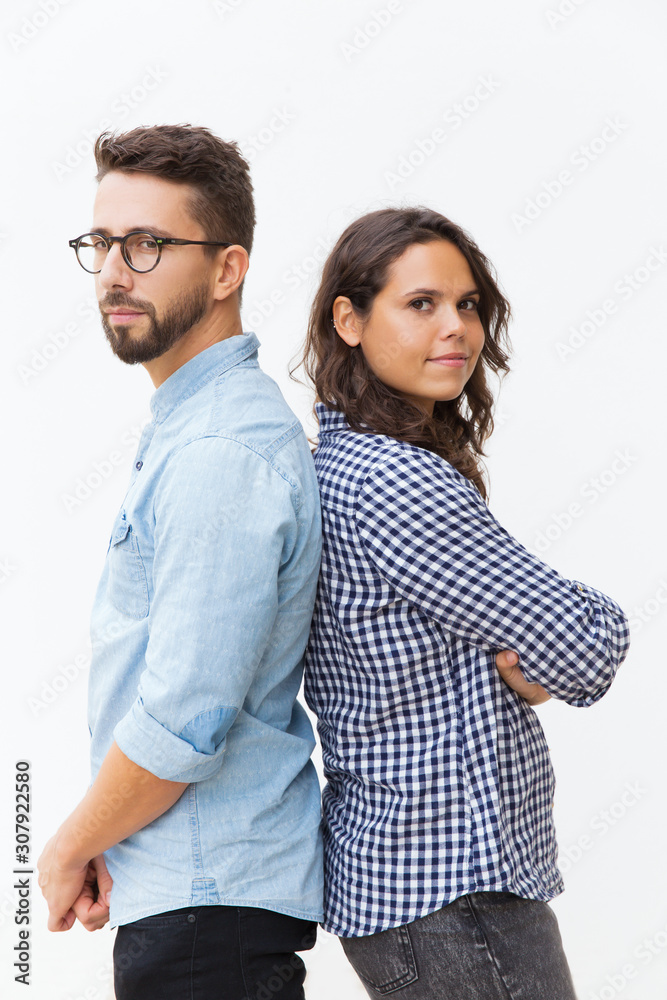 Serious pensive couple standing back-to-back, looking at camera. Young woman in casual and man in glasses in glasses posing isolated over white background. Relationship and support concept Serious pensive couple standing back-to-back, looking at camera. Young woman in casual and man in glasses in glasses posing isolated over white background. Relationship and support concept