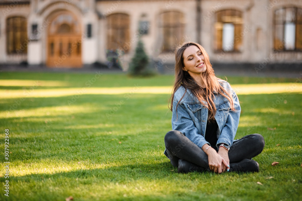 Obraz premium Portrait of a young woman sitting on the green grass in the autumn park
