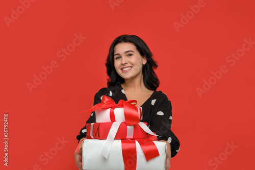 Pretty girl is excited holding several giftboxes of different sizes of white color with red ribbon.