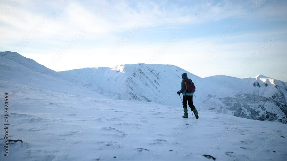 Male mountaineer with trekking poles and a backpack walking on mountain ridge. Young man hiking on top of snowy mountain Male mountaineer with trekking poles and a backpack walking on mountain ridge. Young man hiking on top of snowy mountain