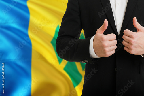 Saint Vincent And The Grenadines businessman showing thumbs up behind country flag with copy space. Successful international relations and agreement concept.