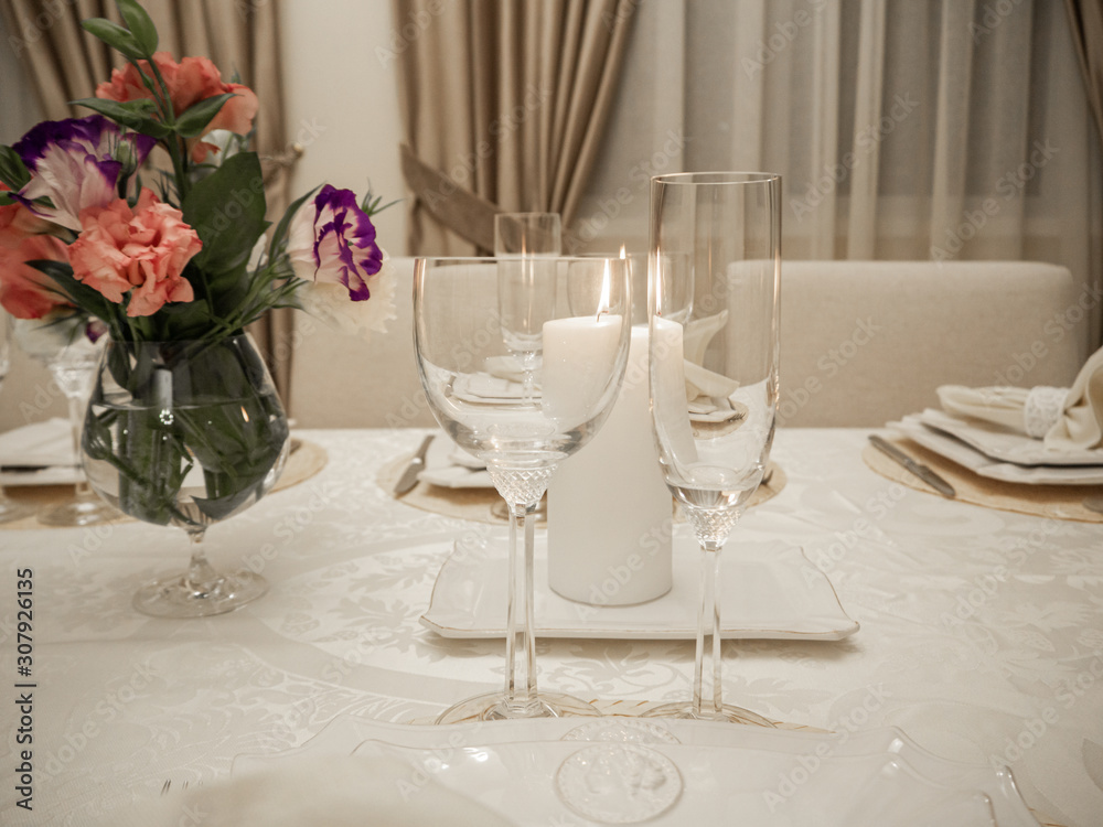 Detail of table setting in beige. Elegant and romantic arrangement for dinner. Сandle, glasses and flowers.