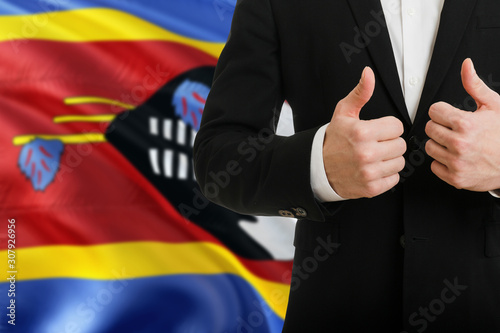 Swaziland businessman showing thumbs up behind country flag with copy space. Successful international relations and agreement concept.