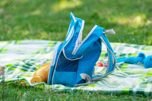 Children's backpack and bottle for water lie on a bedspread on a picnic photo