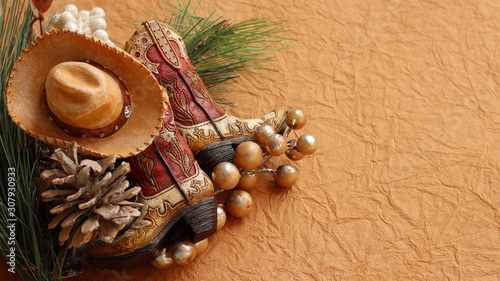Christmas cowboy boots and hat laying with pine cones, rustic berries on a brown textured background with writing space