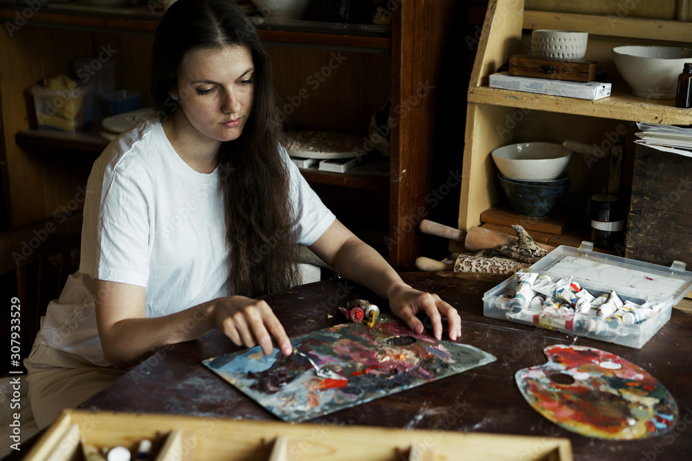 Fototapeta premium Beautiful long-haired woman interferes with a spatula with a palette of oil paints to create a picture. Handwork. Ceramic Making. Wall panel
