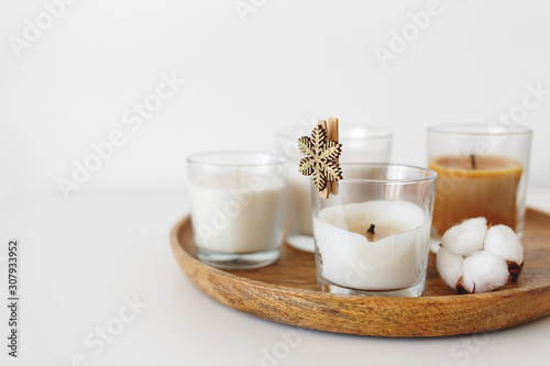 Wooden tray with candles and cotton flowers standing on white table. Cozy home decoration. Interior decor. White background, copy space, selective focus.