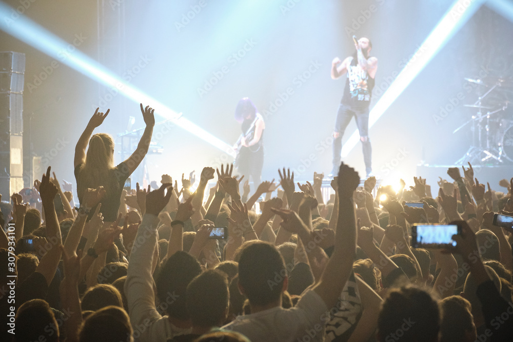 Concert shot, a huge crowd is standing in front of a lit stage clapping