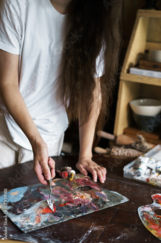 Beautiful long-haired woman interferes with a spatula with a palette of oil paints to create a picture. Handwork. Ceramic Making. Wall panel