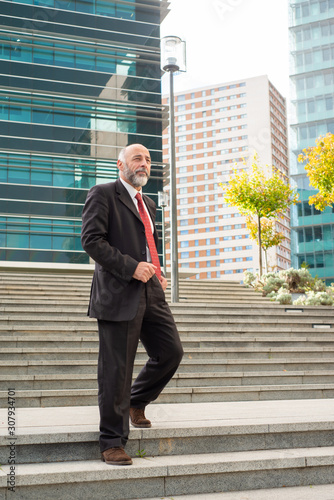 Mature businessman walking down stairs. Low angle view of confident bearded businessman in formal wear walking on stairs and looking aside on urban city street. Business concept
