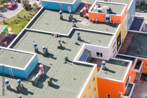 Valokuvatapetti Top view flat roof with air conditioners and hydro insulation membranes on top of a modern blue and orange apartment building sunny summer day