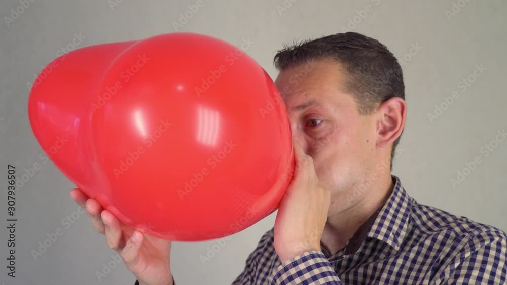 Funny man inflates a red heart-shaped balloon, concept of valentines day and love. Funny man inflates a red heart-shaped balloon, concept of valentines day and love.