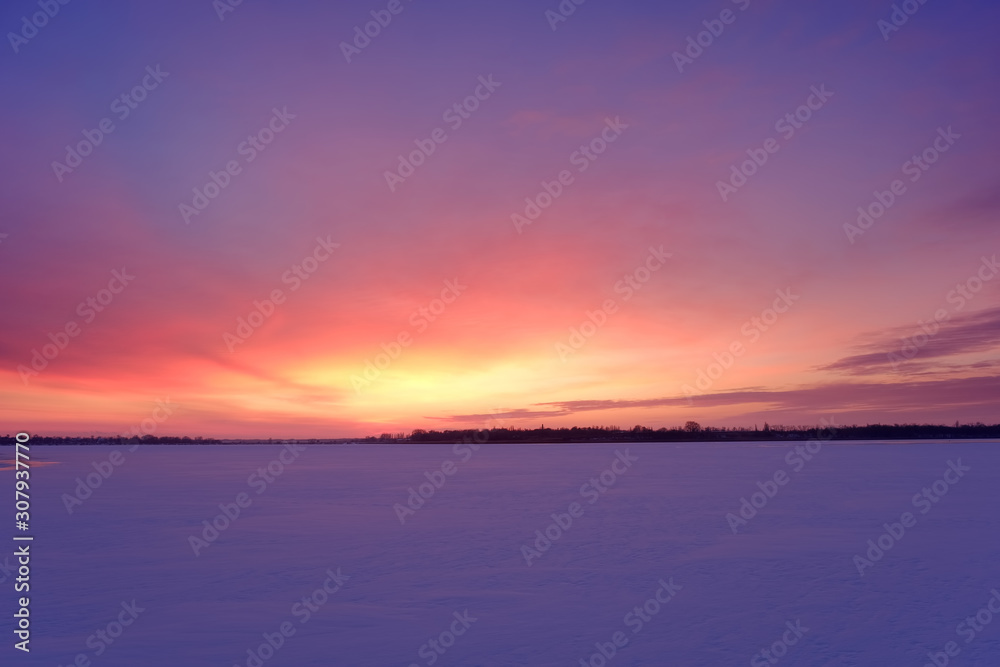 Twilight winter landscape with frozen lake and sunset sky.