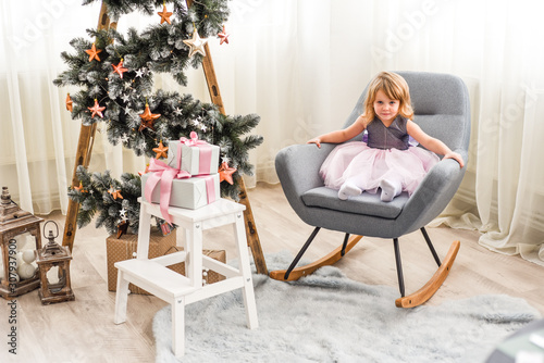 beautiful girl in a pink dress sitting on a chair near a Christmas tree