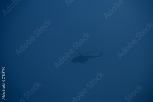 Fototapeta Naklejka Na Ścianę i Meble -  Silhouette of a helicopter flying in a trendy blue sky.