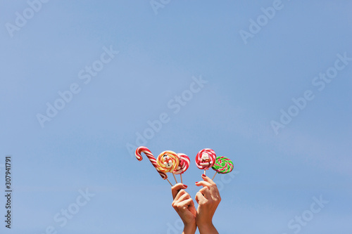 Womens hands holding colored Christmas candies on the blue sky background. Space for text. Christmas concept