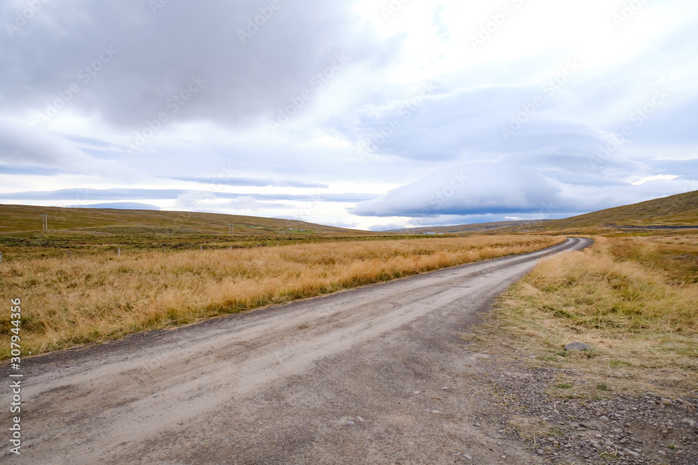 Landscape of Blondus, blue/white sky, grass, a long empty dirt road in pretty autumn colours in Iceland 