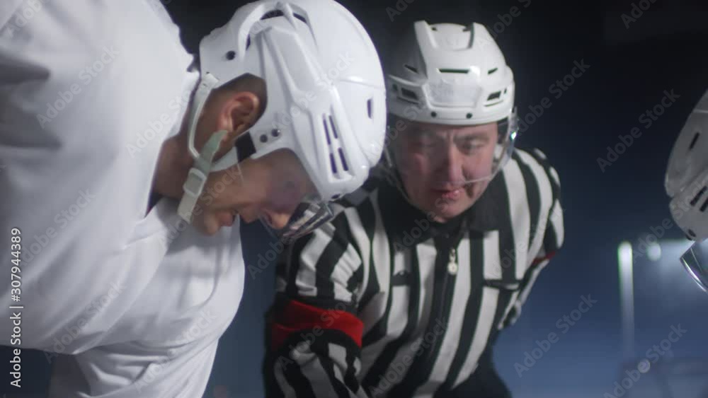 Zoom out shot of referee throwing puck on ice rink, two hockey players from opposing teams standing and waiting for match to begin Zoom out shot of referee throwing puck on ice rink, two hockey players from opposing teams standing and waiting for match to begin
