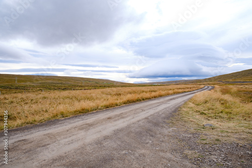 Landscape of Blondus  blue white sky  grass  a long empty dirt road in pretty autumn colours in Iceland 