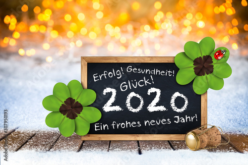 bottle of champagne glasses cork blackboard german greeting frohes neues jahr 2020 greetings (english translation: happy new year 2020 ) card wooden planks front bright golden bokeh light background photo