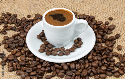 Cup of Greek coffee on sack background with coffee beans. Turkish coffee in white small mug. Traditional Greek coffee concept.