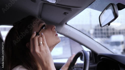 Apply mascara using a brush. Illegal driving. Beautiful young woman looks in the rearview mirror for applying make-up