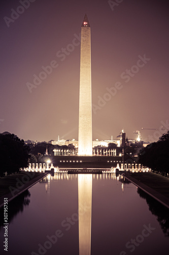 The Washington Monument at night with its image reflected in the National Mall reflecting pool.