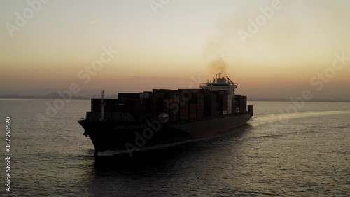 Large Container ship cruising slowly  across the open sea at Sunrise, Aerial follow footage. photo