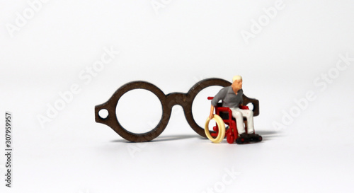 A miniature man in a wheelchair in front of two wooden miniature glasses.