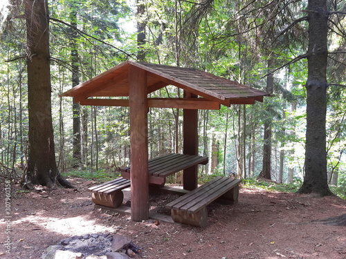 Shelter from wood, with a roof, benches and a fireplace, in the forest