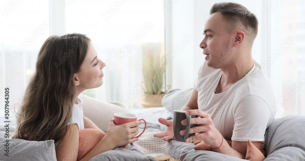 Relaxed young couple drinking coffee while talking in bed at home Relaxed young couple drinking coffee while talking in bed at home