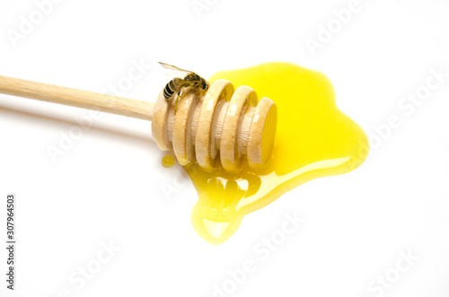 a spoon of honey and a bee over liquid honey on a white