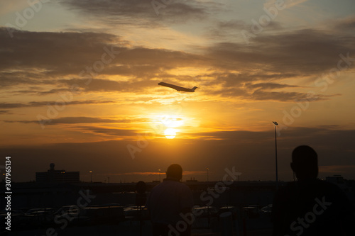 Side silhouette of airplane flying take off over a city during sunset