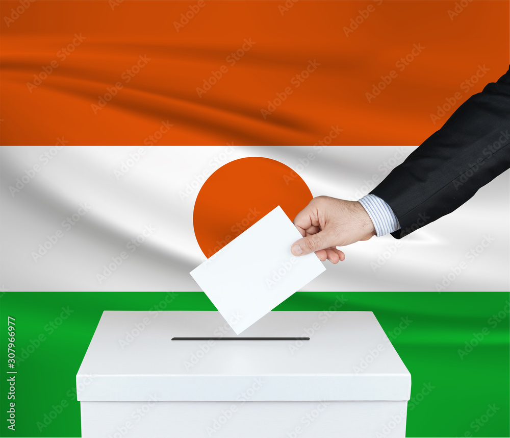 Election in Niger. The hand of man putting his vote in the ballot box. Waved Niger flag on background. Election in Niger. The hand of man putting his vote in the ballot box. Waved Niger flag on background.
