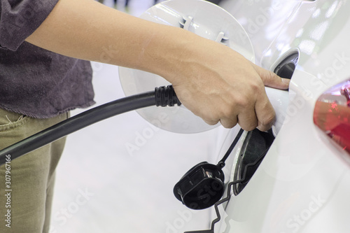 Close-up hand of man who holding a rechargeable machine plug for charger battery on socket of white electric car  Electric power is an alternative fuel for smart vehicles  eco energy