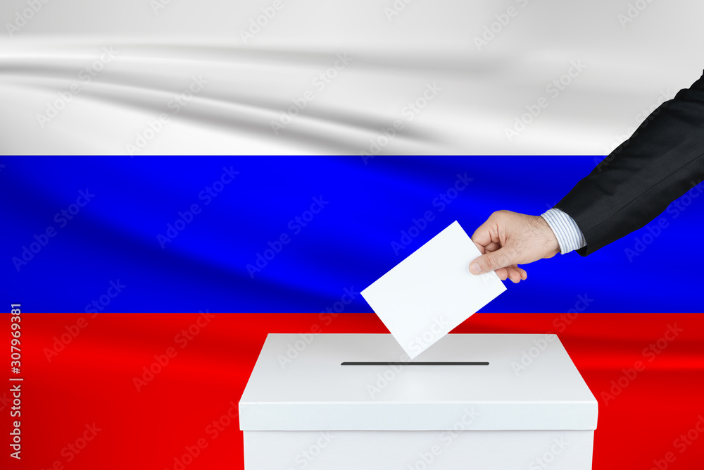 Election in Russia. The hand of man putting his vote in the ballot box. Waved Russia flag on background. Election in Russia. The hand of man putting his vote in the ballot box. Waved Russia flag on background.