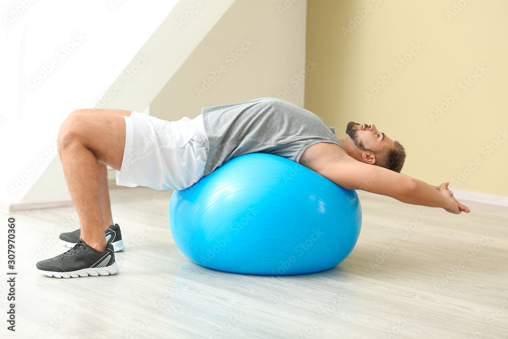 Naklejka premium Sporty young man training with fitball in gym