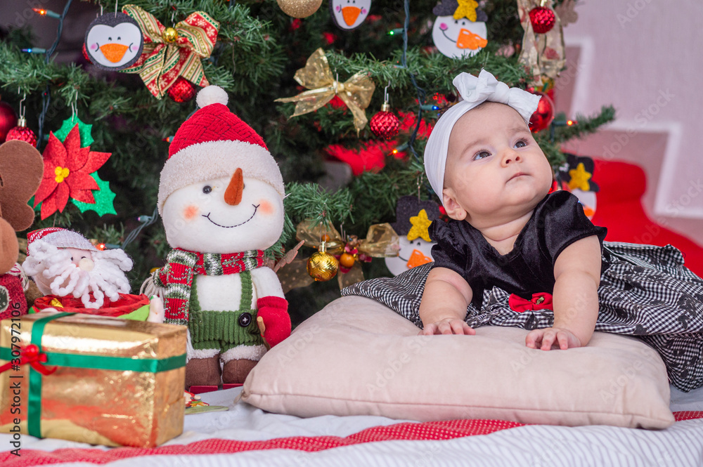 A white baby, Christmas tree decoration with black dress and white bow, on the cushion, look up serious A white baby, Christmas tree decoration with black dress and white bow, on the cushion, look up serious