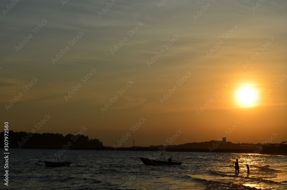 people silhouette play on the beach with the sunset as background and fisherman boat silhouette. in Borneo,Indonesia. people silhouette play on the beach with the sunset as background and fisherman boat silhouette. in Borneo,Indonesia.