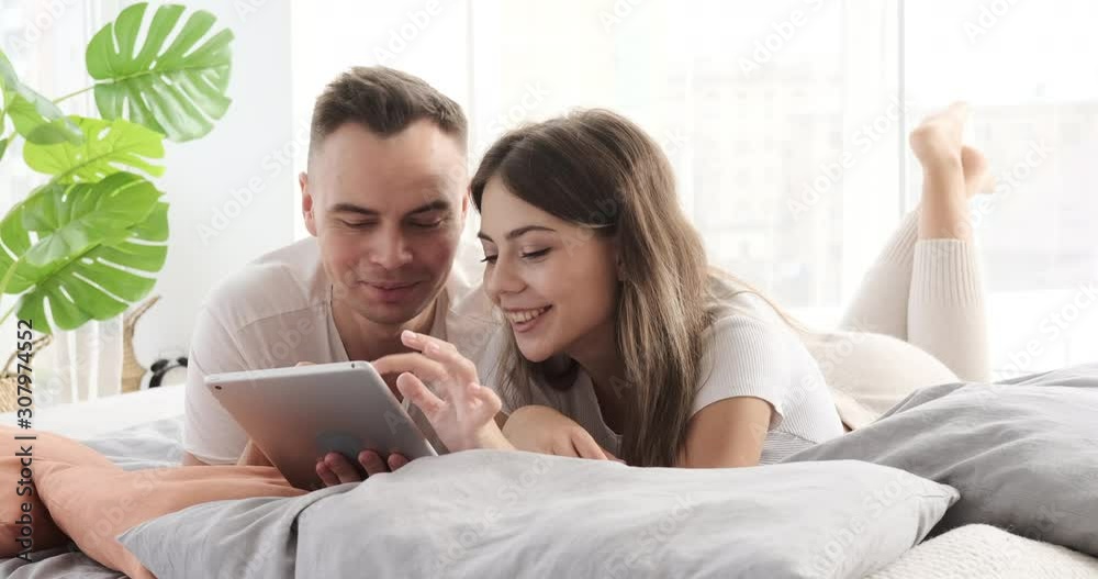 Couple having fun using digital tablet lying on bed at home Couple having fun using digital tablet lying on bed at home