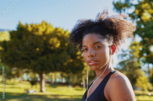 Portrait of a fitness african american young woman with earphones in her ears listening to music at park before doing exercise on a sunny day