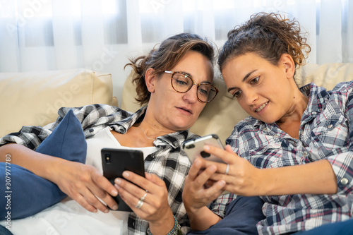 Two girls lying on a couch with mobiles in hand sharing information