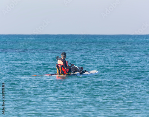 Active elderly man rowing on a surfboard