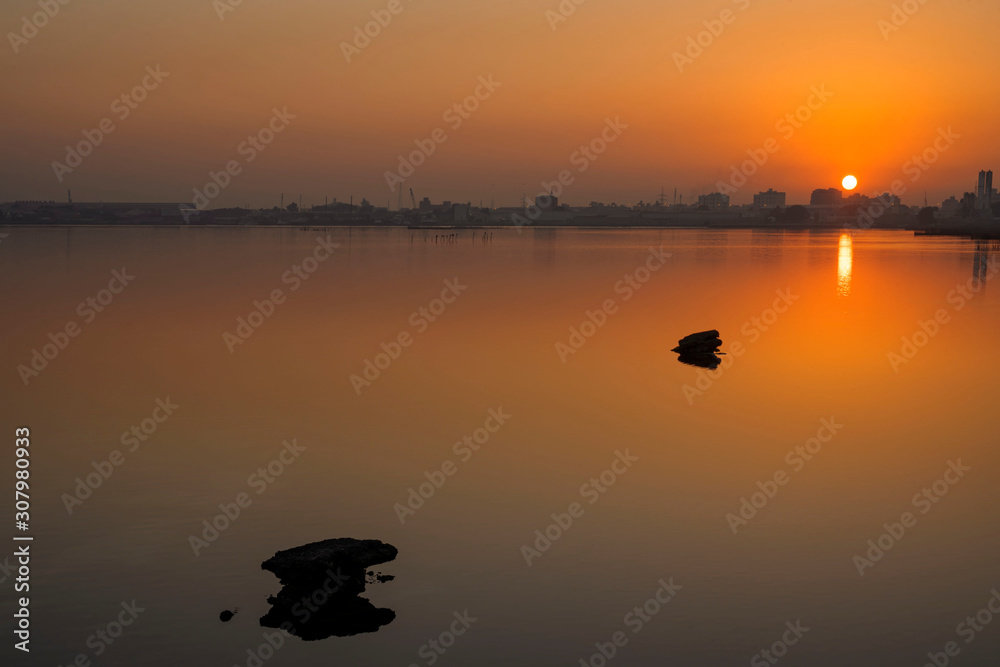 Rocks with reflections on calm water and beautiful sunrise over colorful sky with silhouette background, Bahrain.
