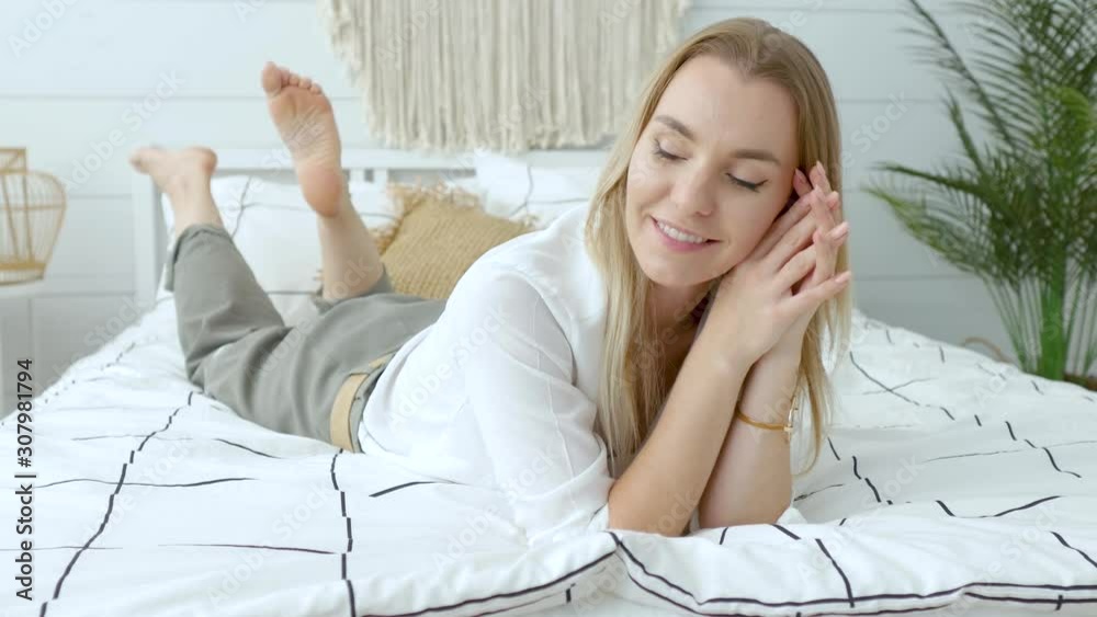 charming smiling woman in a shirt and trousers lies on a bed in a bright bedroom charming smiling woman in a shirt and trousers lies on a bed in a bright bedroom