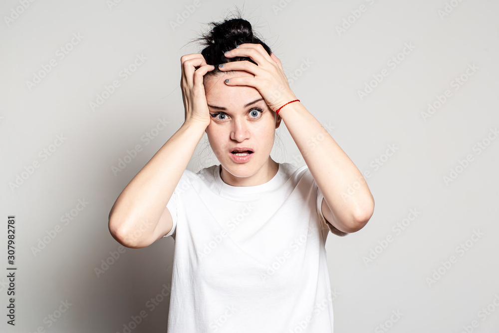 Young woman in despair and panic keeps hands on her head, opens mouth in bewilderment and looks anxiously into the camera with big eyes. Young woman in despair and panic keeps hands on her head, opens mouth in bewilderment and looks anxiously into the camera with big eyes.