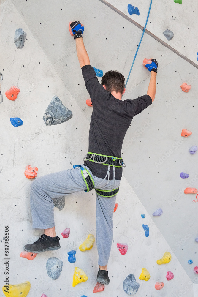 A man climbs up on a climbing wall.