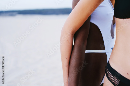Fototapeta Naklejka Na Ścianę i Meble -  Hands of African and European models female wearing swimsuit together on sea shore
