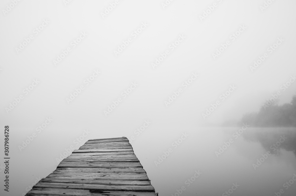 Fototapeta premium Wooden footbridge on lake with thick mist foggy air over water. Early chilly morning in late autumn. Empty place(copyspace) for text, quote or sayings. Concepts: peaceful, mindfullness, secret, nature